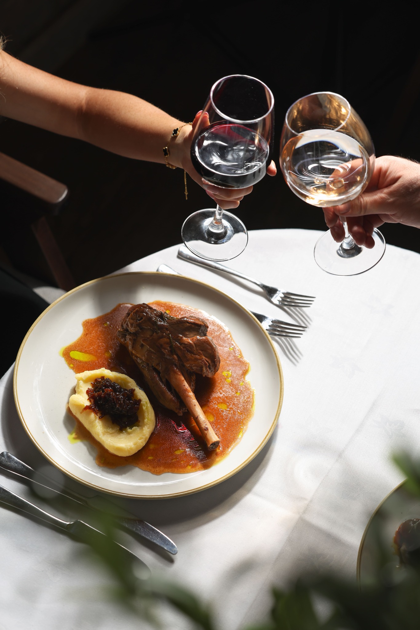 Two guests raise red and white wine over a lamb dish at Yammas in Beckenham